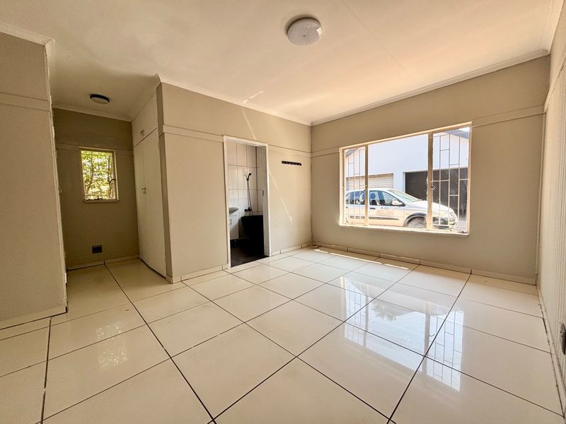 A bright, empty bedroom featuring neutral tiled flooring, built-in cupboards, and large windows with security bars, offering a clean and functional living space.