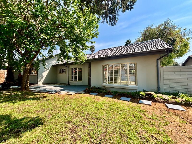 Rear view of the house featuring a tiled roof, bay windows with security bars, and a paved patio area set within a garden.