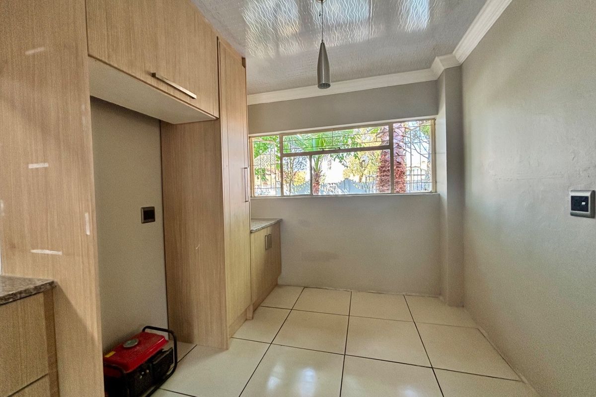 A clean, functional kitchen area featuring light wood-toned built-in cabinetry, stone countertops, and large format floor tiles with natural light from the window.