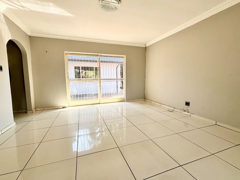 A bright, empty living room featuring polished white floor tiles, crown molding, and a sliding glass door with security gate leading to the exterior.