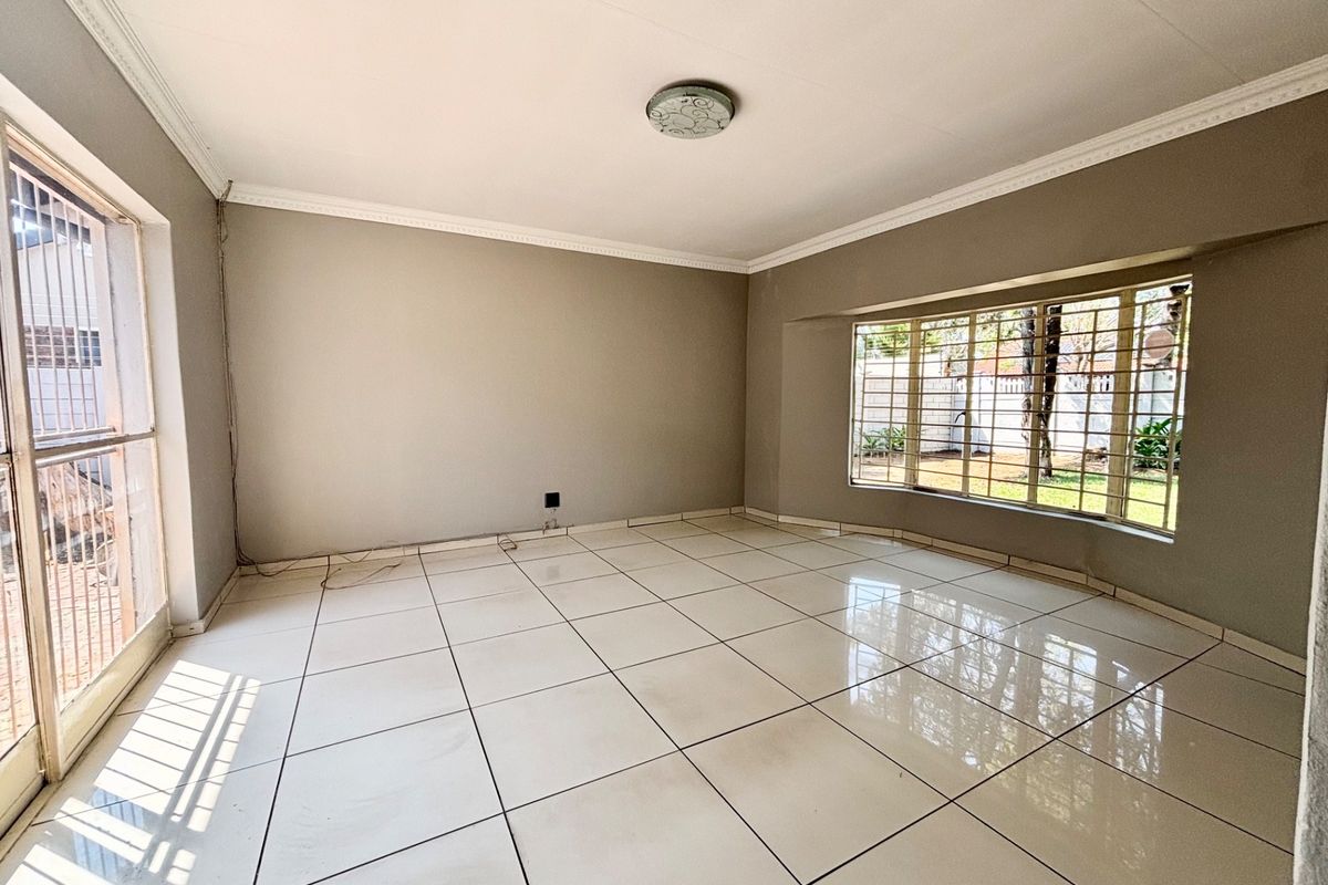 A spacious, empty living room featuring large tiled floors, a bay window with security bars, and a sliding door leading to the exterior.