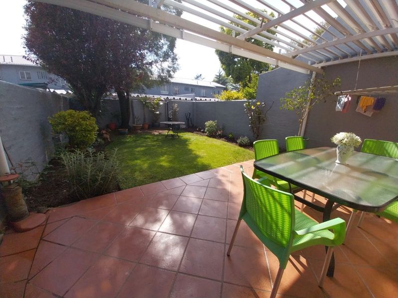 A private outdoor patio featuring tiled flooring and a slatted pergola, overlooking a small, well-maintained garden area with boundary walls.