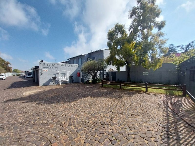 Front entrance view of the Barcelona townhouse complex featuring a cobblestone driveway, perimeter walling, and established landscaping.