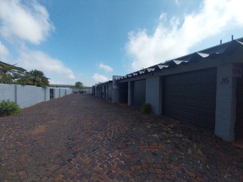 A view of the townhouse complex driveway featuring a row of garages with dark doors and a cobblestone paved surface.