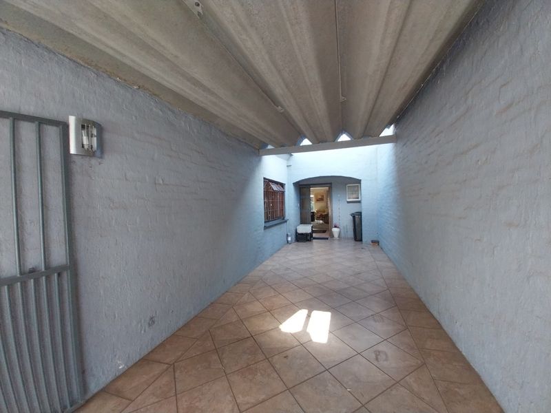 A covered outdoor patio area featuring tiled flooring, a corrugated roof, and a security gate, providing a functional transition space to the interior.