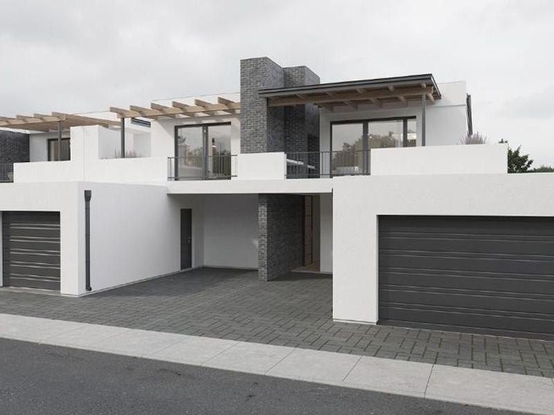 Modern townhouse complex featuring clean white facades, dark brick accents, timber pergolas, and multiple integrated garage doors with paved driveway access.