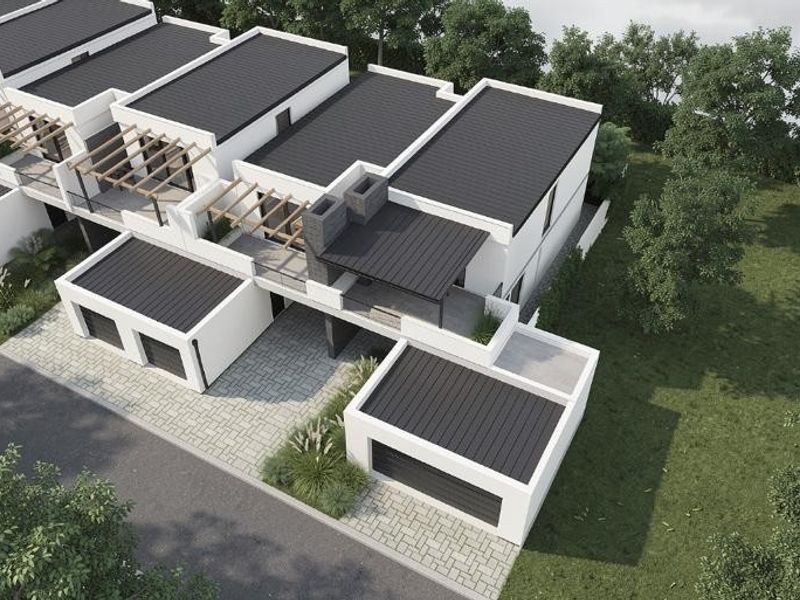 Aerial view of a modern townhouse development featuring clean architectural lines, flat roofs, integrated garages, and paved driveways set within a landscaped environment.