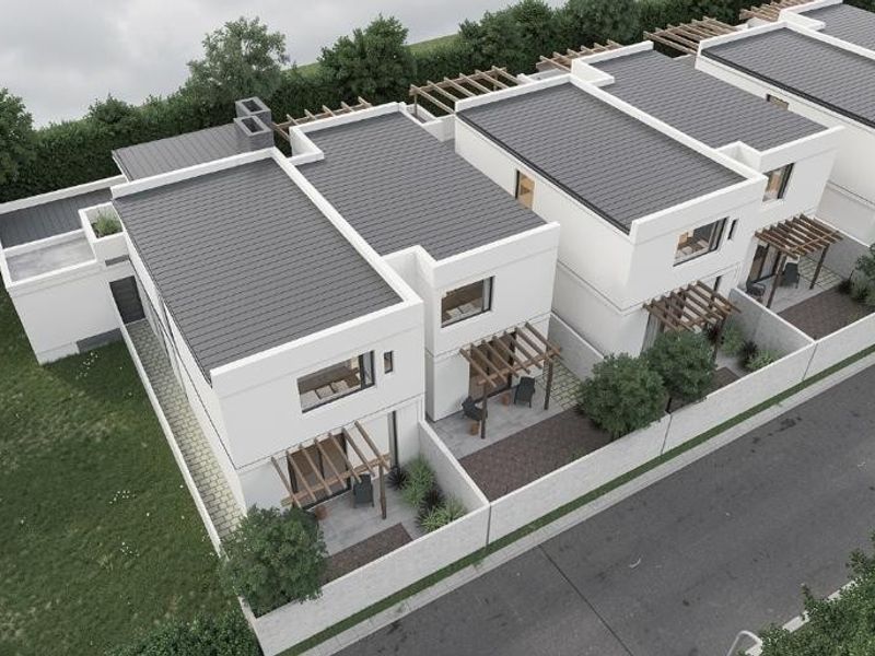 An aerial view of a modern residential townhouse complex featuring clean white facades, dark pitched roofs, and private patio areas with timber pergolas.