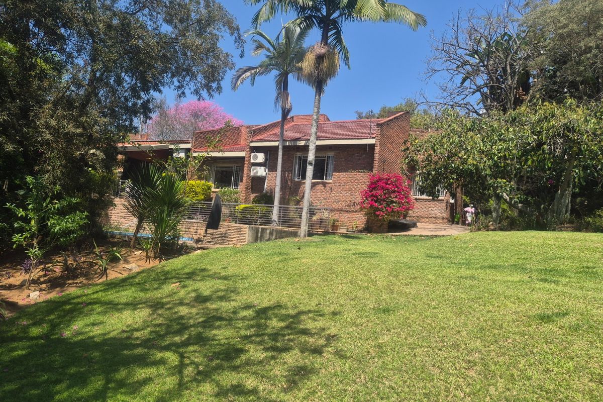 Rear view of a brick house featuring a tiled roof, air conditioning unit, and a spacious, well-maintained garden with mature trees.