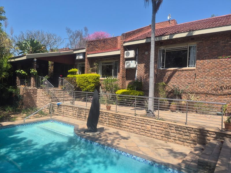 A well-maintained outdoor pool area featuring a tiled patio, stone retaining walls, and a modern stainless steel balustrade overlooking the swimming pool.