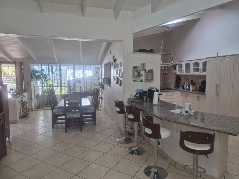 Open-plan living and dining area featuring a functional kitchen with granite countertops, breakfast bar, and exposed beam ceilings, creating a spacious, connected layout.