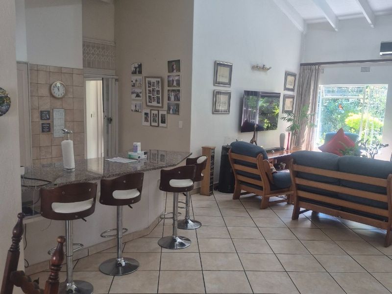 Open plan living area featuring tiled flooring, a granite breakfast counter, and a spacious vaulted ceiling with exposed beams leading to the garden.