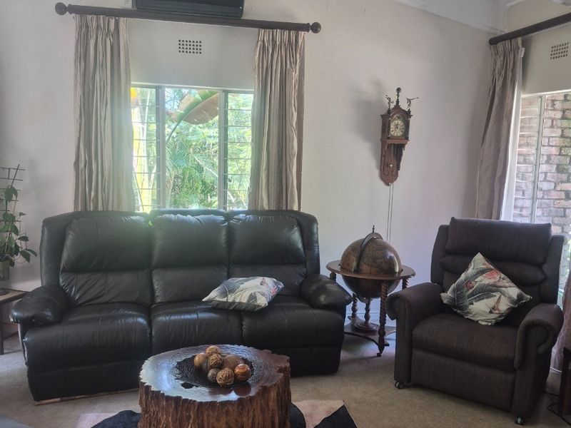 A living room featuring a vaulted ceiling with exposed beams, carpeted flooring, and a wall-mounted split-system air conditioner.