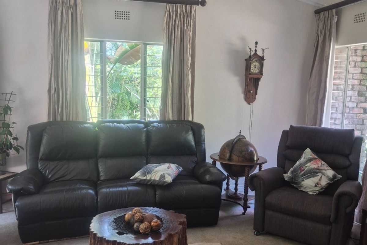 A living room featuring a vaulted ceiling with exposed beams, carpeted flooring, and a wall-mounted split-system air conditioner.