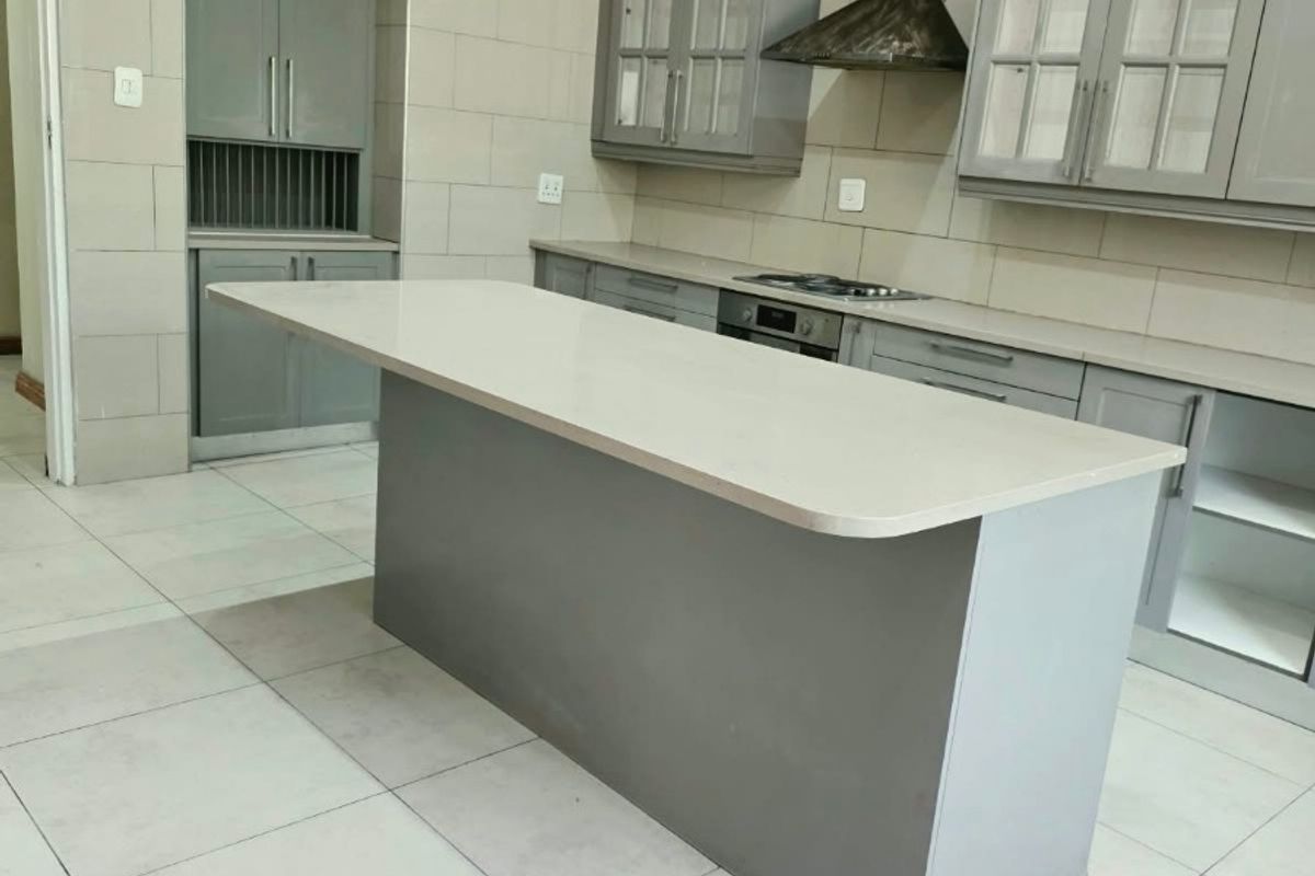 Modern kitchen featuring a central island, grey cabinetry, stone countertops, and integrated appliances, currently awaiting final finishing touches.