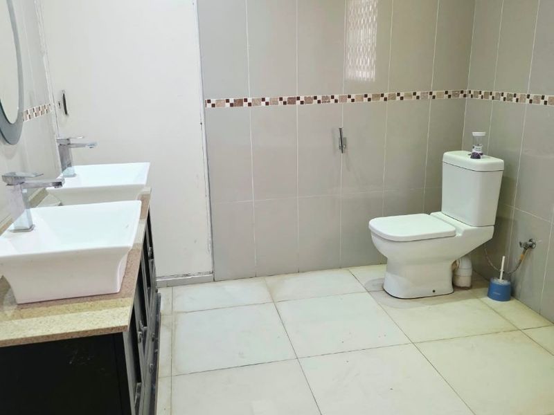 A clean, modern bathroom featuring a double vanity with vessel sinks, granite countertops, and neutral floor-to-ceiling wall tiles.