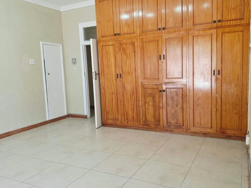 A spacious, empty bedroom featuring extensive floor-to-ceiling built-in wooden cabinetry, neutral tiled flooring, and modern track lighting.