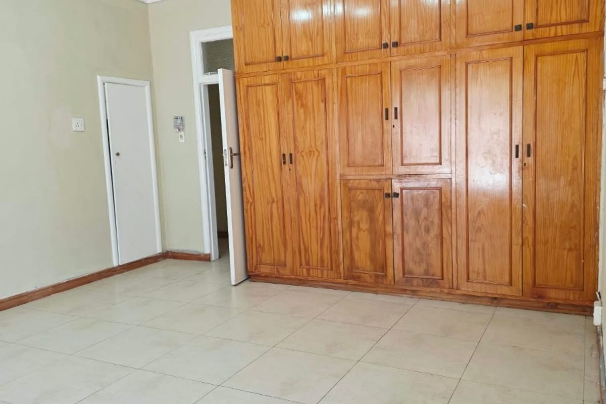 A spacious, empty bedroom featuring extensive floor-to-ceiling built-in wooden cabinetry, neutral tiled flooring, and modern track lighting.
