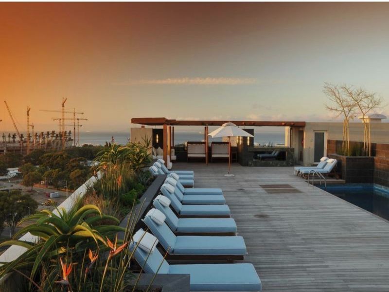 A rooftop pool area featuring timber decking, built-in seating, and landscaped planters, offering expansive views of the surrounding area.