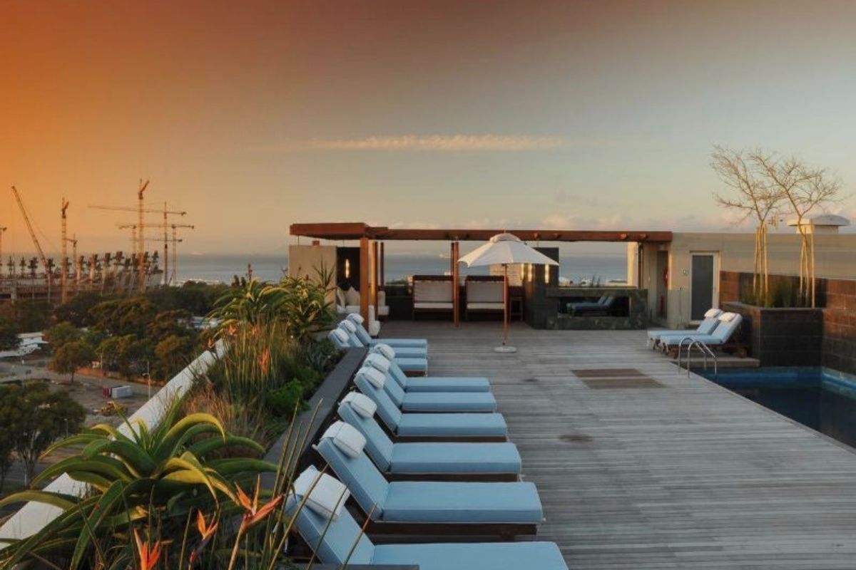 A rooftop pool area featuring timber decking, built-in seating, and landscaped planters, offering expansive views of the surrounding area.