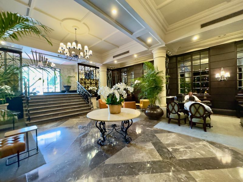Elegant apartment building lobby featuring high coffered ceilings, polished marble flooring, a grand staircase, and a professional reception area.