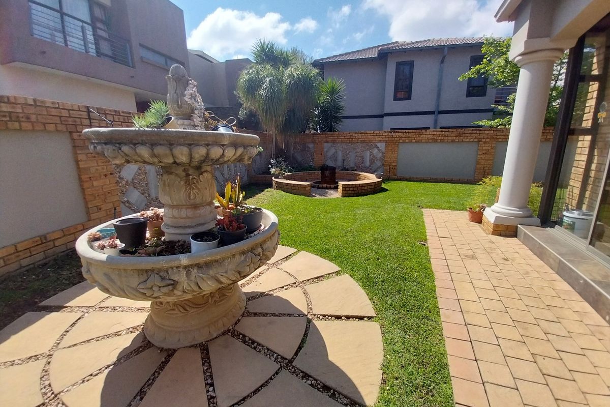 A private rear garden featuring a paved patio area, a central stone fountain, and a built-in brick fire pit surrounded by a lawn.