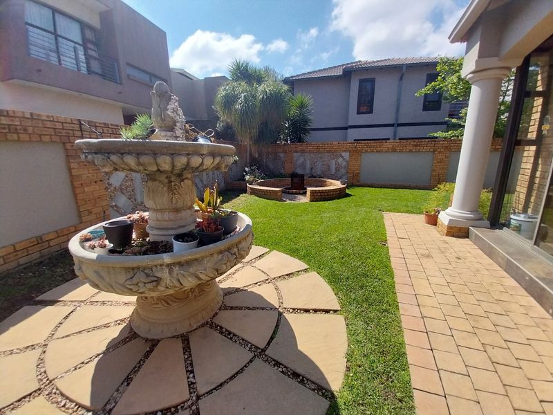 A private rear garden featuring a paved patio area, a central stone fountain, and a built-in brick fire pit surrounded by a lawn.
