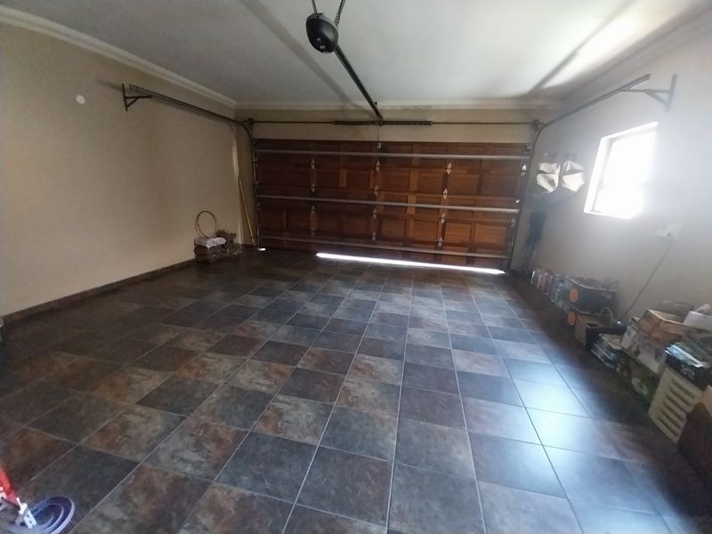 A spacious double garage featuring tiled flooring and a functional sectional garage door with an automated motor system.