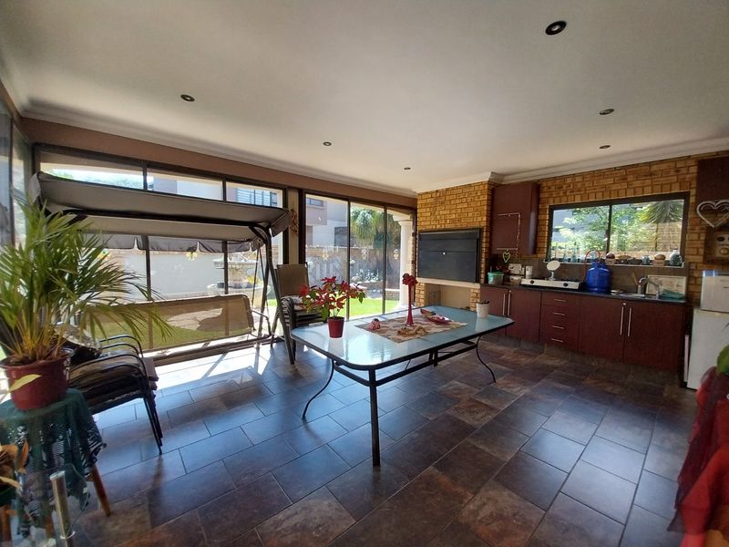 Enclosed patio area featuring a built-in braai, kitchenette with cabinetry and sink, tiled flooring, and large sliding glass doors opening to the garden.