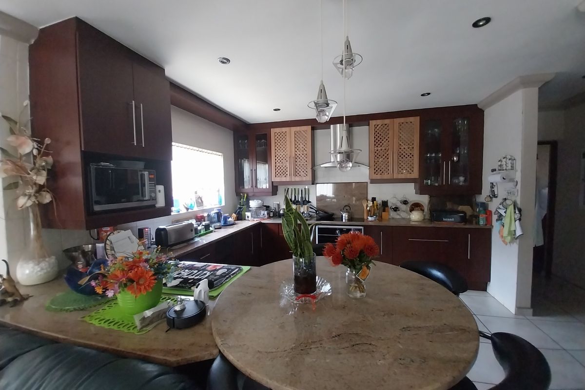 A functional kitchen featuring dark wood cabinetry, stone countertops, integrated appliances, and a central breakfast bar area with pendant lighting.