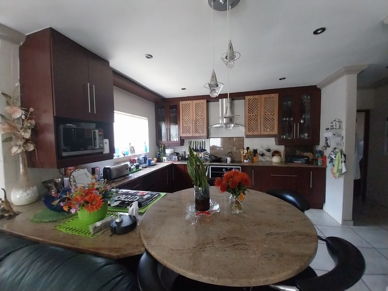 A functional kitchen featuring dark wood cabinetry, stone countertops, integrated appliances, and a central breakfast bar area with pendant lighting.