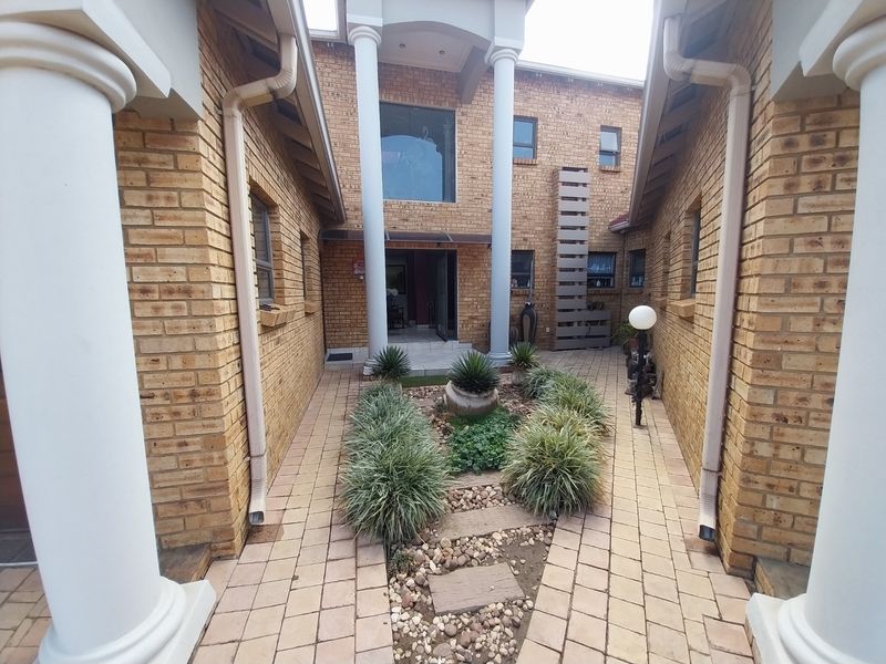 Front entrance courtyard featuring face brick walls, classical columns, and a paved walkway leading to the main doorway.