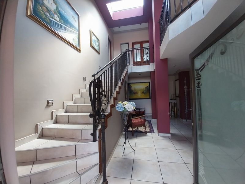 Spacious double-volume entrance hall featuring a tiled staircase with wrought iron balustrade and a large skylight providing natural light.
