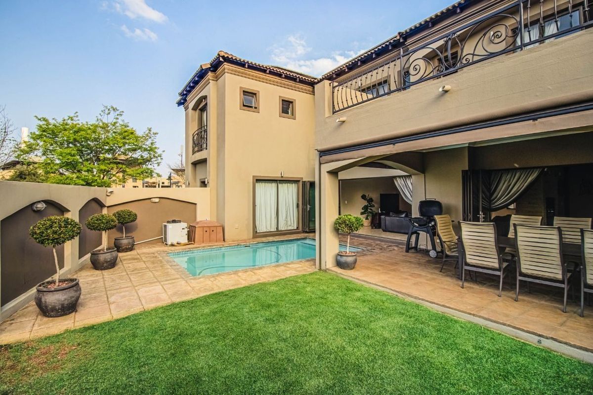 Rear exterior view featuring a swimming pool, covered patio area, and a manicured lawn with a balcony above.