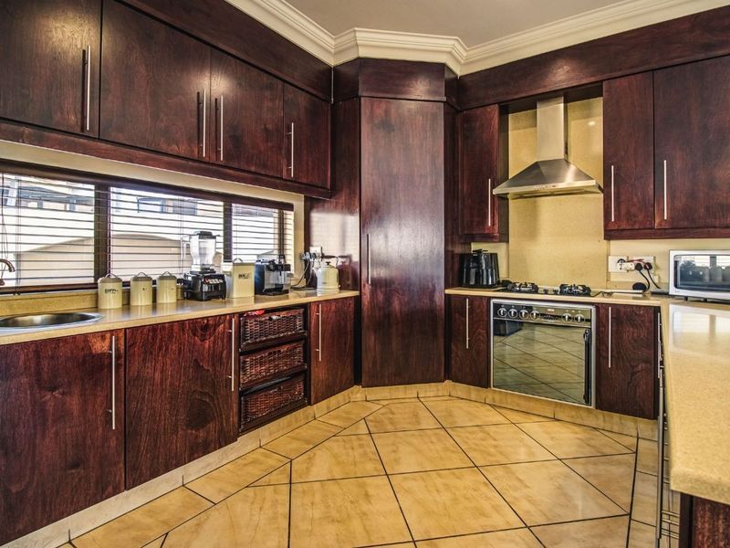 A well-maintained kitchen featuring dark wood cabinetry, stone countertops, integrated stainless steel appliances, and tiled flooring with decorative inlay.