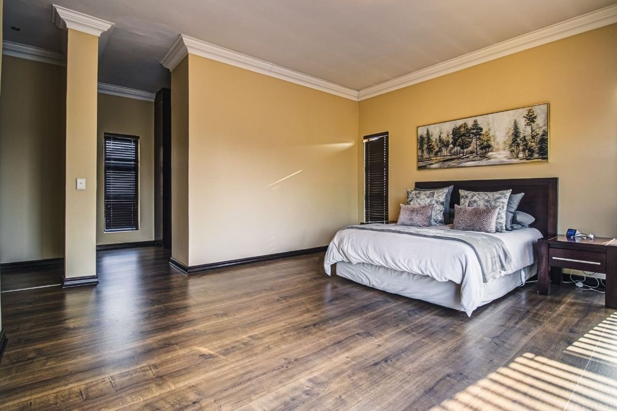 Spacious bedroom featuring dark laminate flooring, crown molding, and venetian blinds, offering a clean and well-maintained living space.