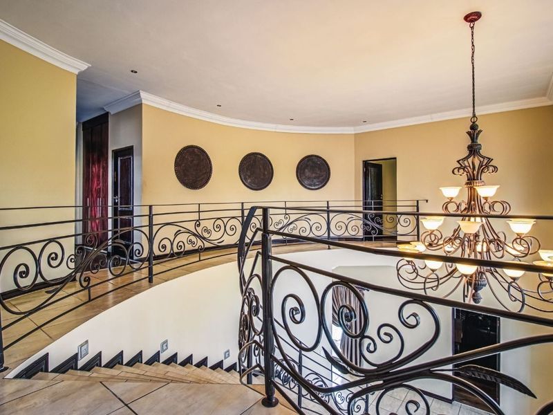 Spacious upper-level landing featuring an elegant wrought iron balustrade, decorative chandelier, and neutral tiled flooring with access to multiple rooms.