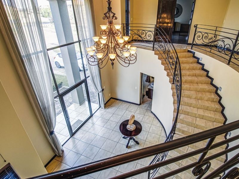 Grand double-volume entrance hall featuring a sweeping staircase with wrought iron balustrades, large floor-to-ceiling windows, and a decorative chandelier.