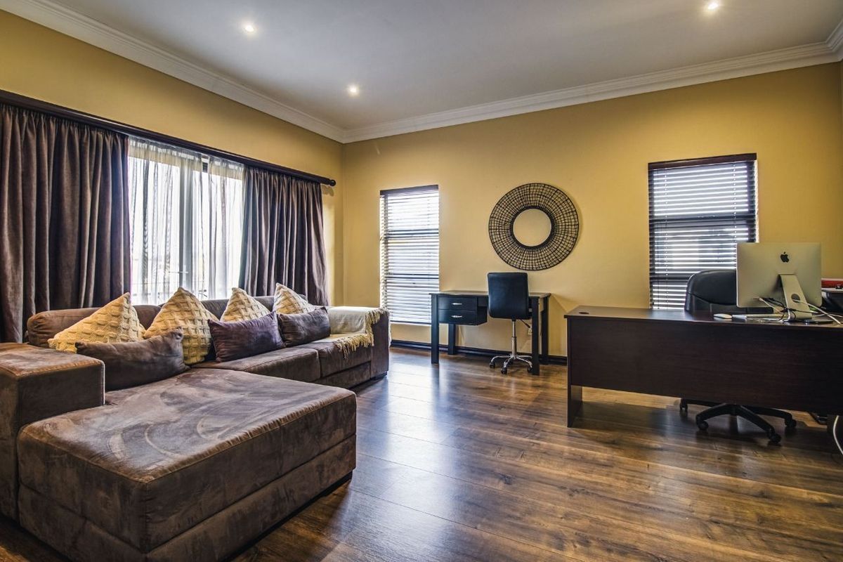 A spacious living area featuring warm-toned laminate flooring, recessed downlighting, and large windows fitted with venetian blinds and curtain tracks.