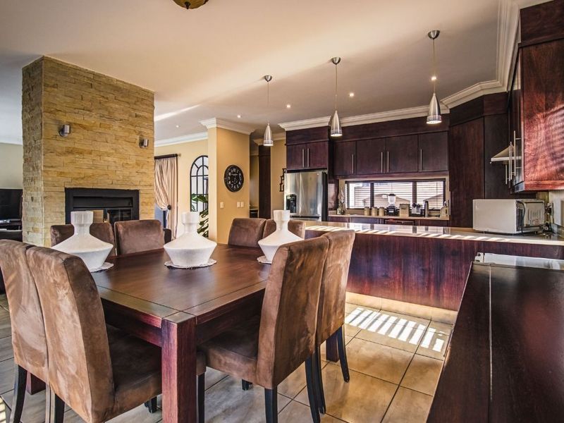 Open-plan living and dining area featuring a stone-clad fireplace, dark wood cabinetry, kitchen island, and modern pendant lighting.