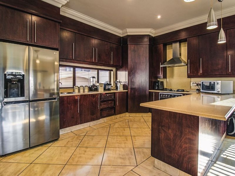 Spacious kitchen featuring dark wood cabinetry, stone countertops, stainless steel appliances, and tiled flooring with recessed lighting.