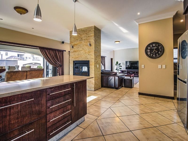 Spacious open-plan living area featuring a central stone-clad fireplace, modern kitchen cabinetry with stone countertops, and seamless flow to the outdoor patio.