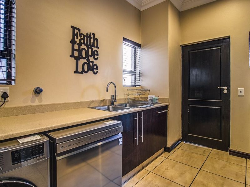 A functional laundry room featuring dark wood cabinetry, stone countertops, a stainless steel sink, and tiled flooring with direct access to an adjacent room.