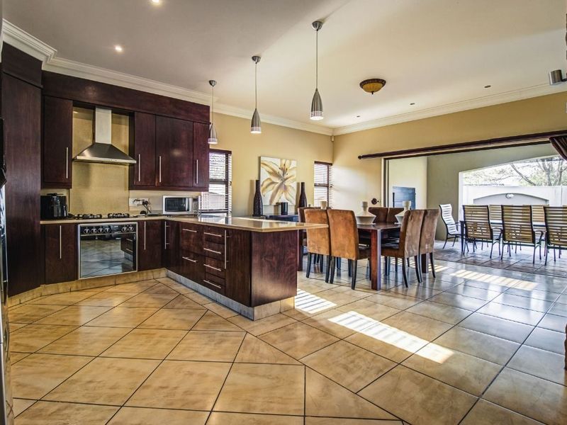 Spacious open-plan kitchen and dining area featuring dark wood cabinetry, stone countertops, tiled flooring, and seamless access to the outdoor patio.