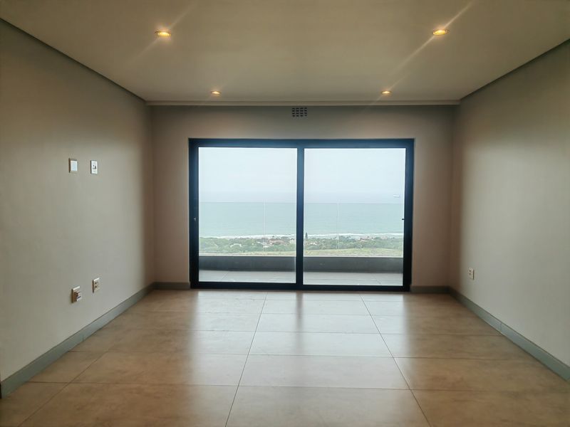 An empty, well-maintained living area featuring large sliding glass doors that provide natural light and expansive ocean views.