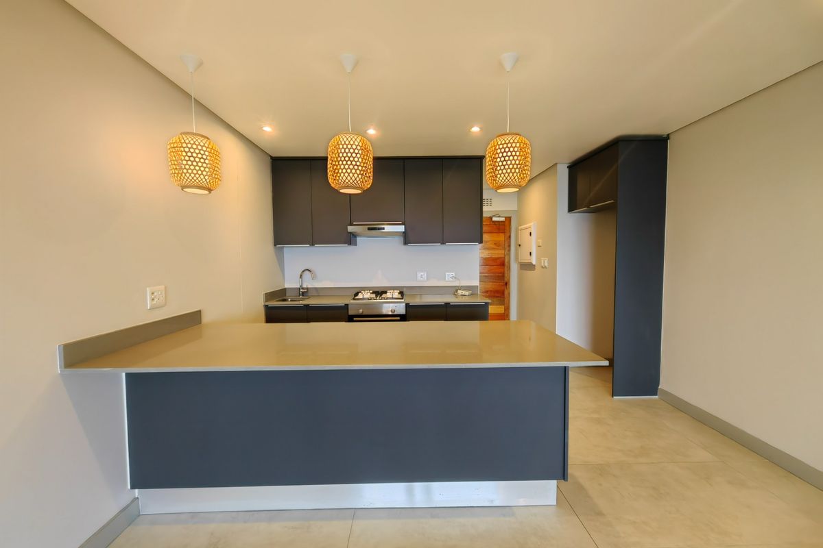 Modern kitchen featuring dark cabinetry, stone countertops, a gas hob with extractor, and stylish pendant lighting, offering a clean and functional culinary space.