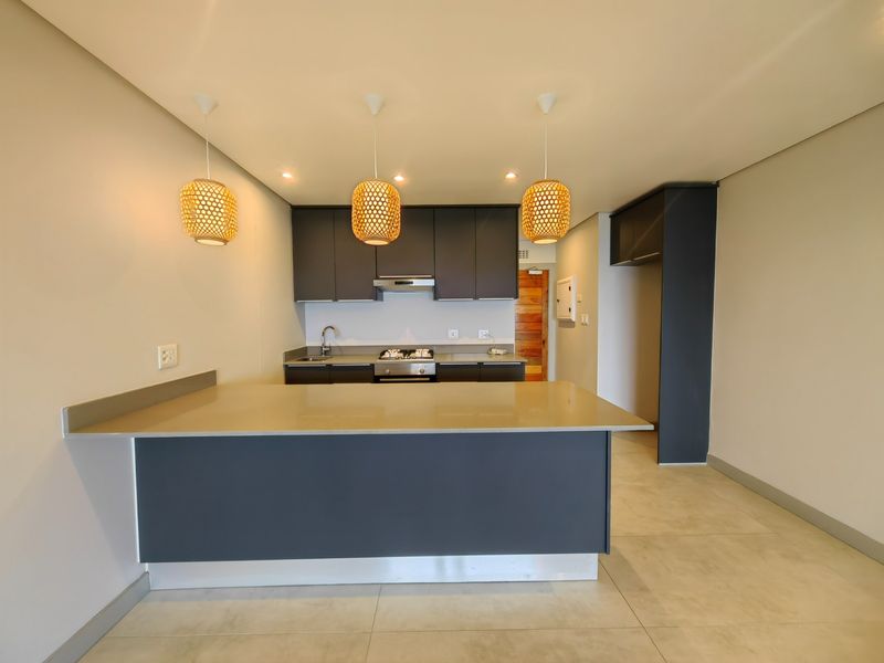 Modern kitchen featuring dark cabinetry, stone countertops, a gas hob with extractor, and stylish pendant lighting, offering a clean and functional culinary space.