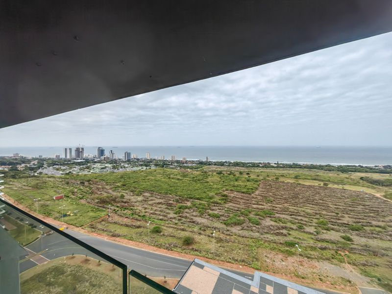 Elevated panoramic view overlooking the coastline, urban skyline, and surrounding landscape from a high-rise apartment balcony.