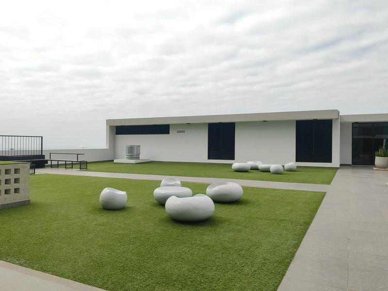 A spacious rooftop terrace featuring artificial turf, paved walkways, and modern metal railings, providing an open-air communal area.