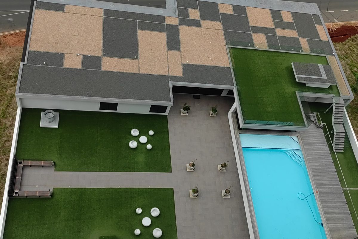 Aerial view of a modern apartment complex featuring a swimming pool, landscaped artificial turf areas, paved courtyard, and outdoor decking.